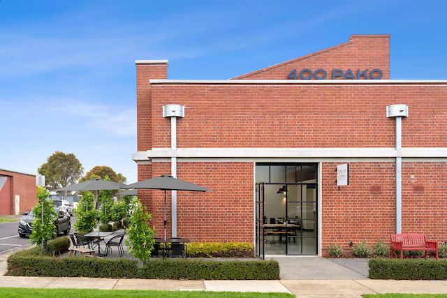 Corner cafe in a red brick building with outdoor tables arranged along the sidewalk. Large windows and greenery add to the inviting, urban space created by Hamilton group Geelong