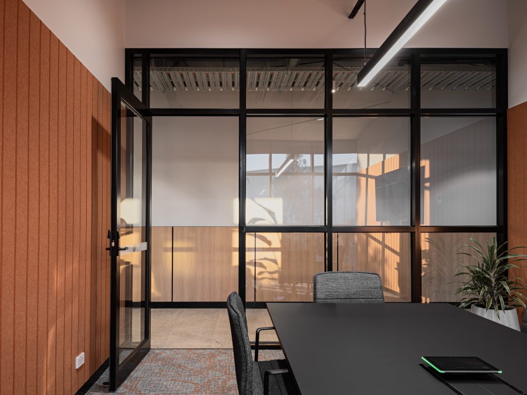 Office fit-out in Laverton North by Hamilton Group. Boardroom with terracotta panelling, large glass windows, black table and swivel chairs. 