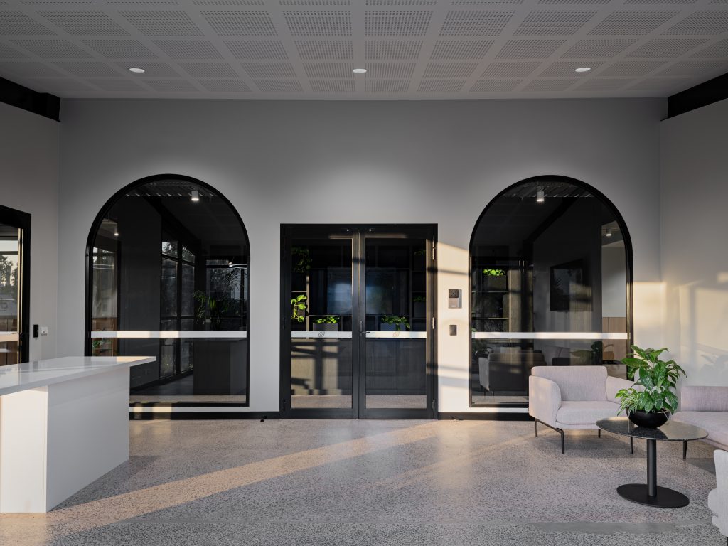 Office fit-out in Laverton North by Hamilton Group. Office entrance / foyer. Beautiful arch windows, white counter and grey sofa chair and couch.